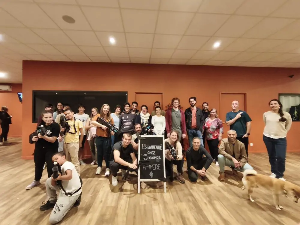 Groupe de plus de vingt collègues avec leurs blasters VR devant l'ardoise « Bienvenue chez Oxmoz » à Blagnac